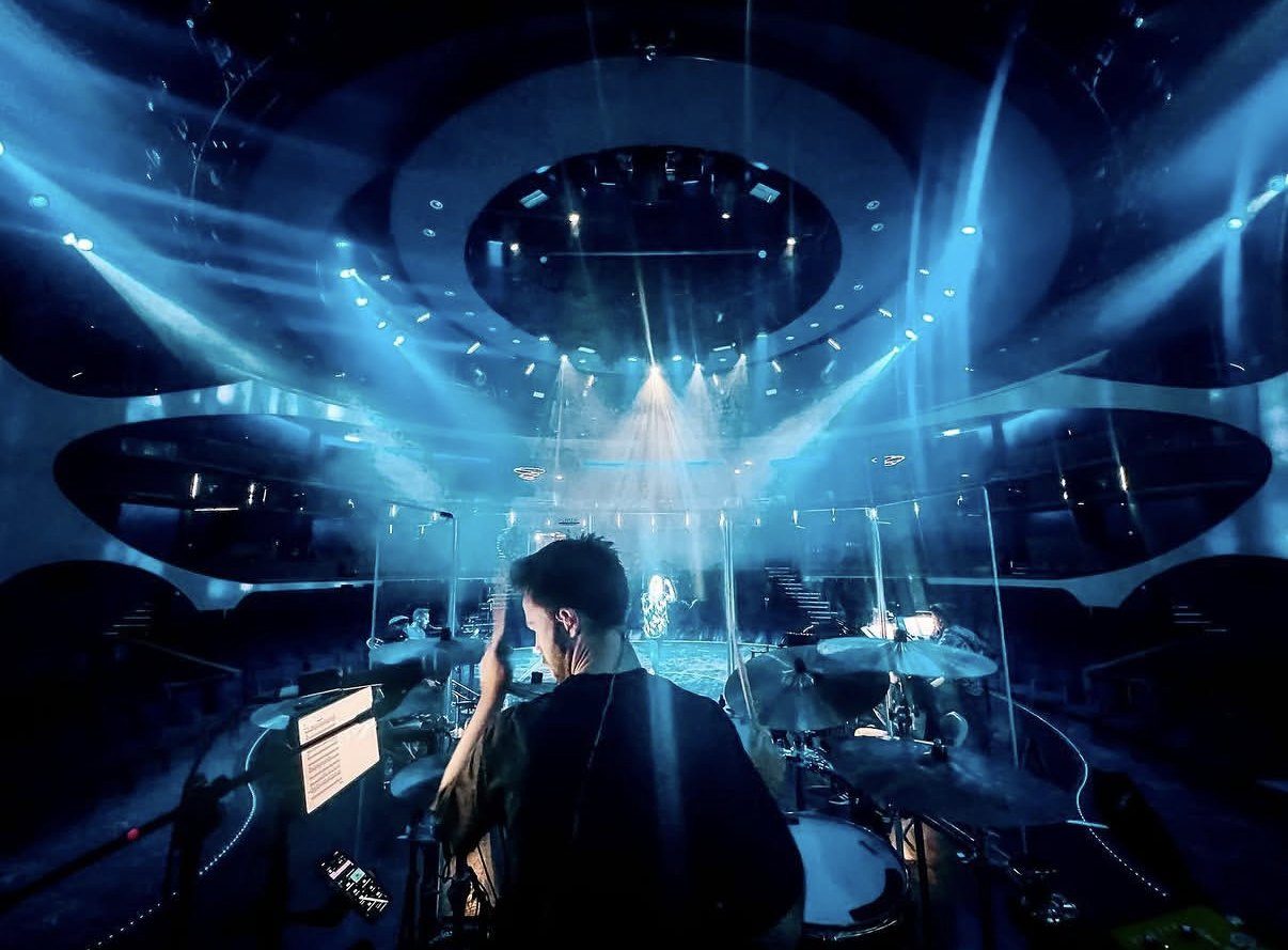 View from behind Oli at the kit, looking out over a theatre lit with blue beams